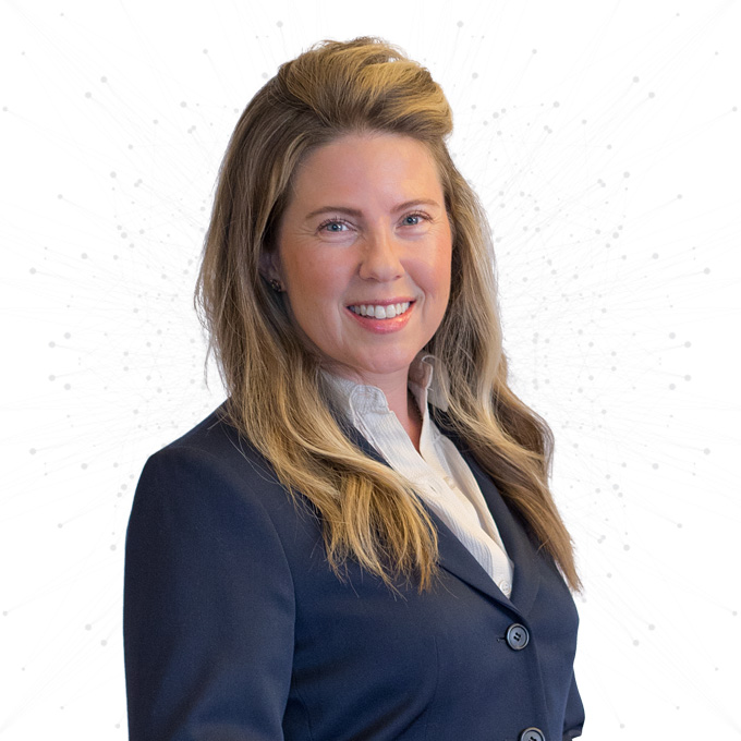 A woman with long, light brown hair wearing a navy blazer and white blouse smiles at the camera against a white background with a subtle dotted pattern.