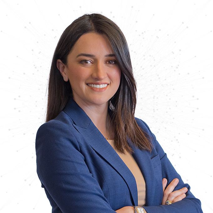 A woman with long dark hair wearing a blue blazer and beige top stands with her arms crossed, smiling confidently against a white background with subtle dotted network patterns.