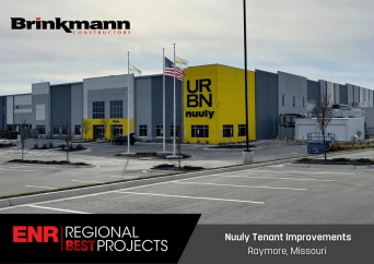 Modern industrial building with yellow URBN nuuly signage, two flagpoles, and an empty parking lot. Text reads: ENR Regional Best Projects - Nuuly Tenant Improvements, Raymore, Missouri, Brinkmann Constructors.