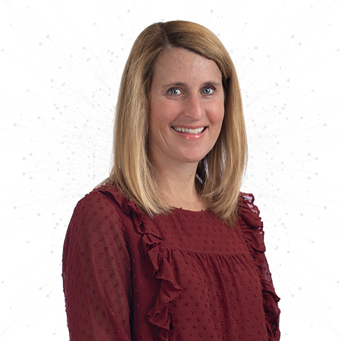 A woman with straight, shoulder-length blonde hair is smiling and wearing a maroon blouse with ruffle details. The background is white with a subtle pattern of dotted lines.