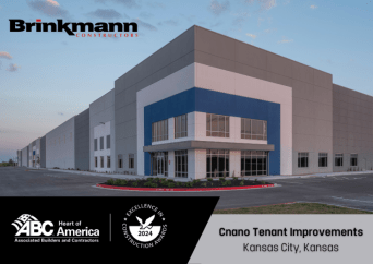 A large, modern industrial building with gray and blue accents is shown. Logos for Brinkmann Constructors, ABC Heart of America, and an Excellence in Construction award are visible, with text reading Cnano Tenant Improvements, Kansas City, Kansas.