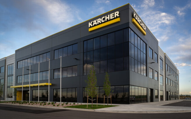 A modern, three-story office building with large glass windows and a yellow Kärcher sign on the corner. The area is landscaped with small trees and the sky is partly cloudy.