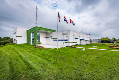 A modern white and green building with three flagpoles outside, displaying the U.S., Missouri, and another flag. The sign reads St. Charles County. The building is surrounded by a well-kept lawn and a cloudy sky above.