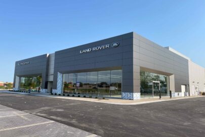 A modern Land Rover dealership building with large windows and a minimalist gray exterior, located on a paved lot under a clear blue sky.