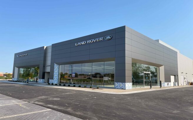 A modern Land Rover dealership building with large windows and a minimalist gray exterior, located on a paved lot under a clear blue sky.
