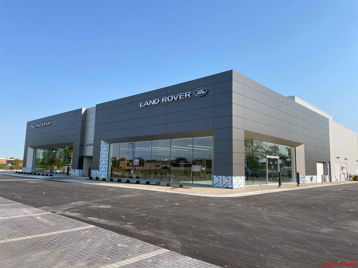 A modern Land Rover dealership building with large windows and a minimalist gray exterior, located on a paved lot under a clear blue sky.