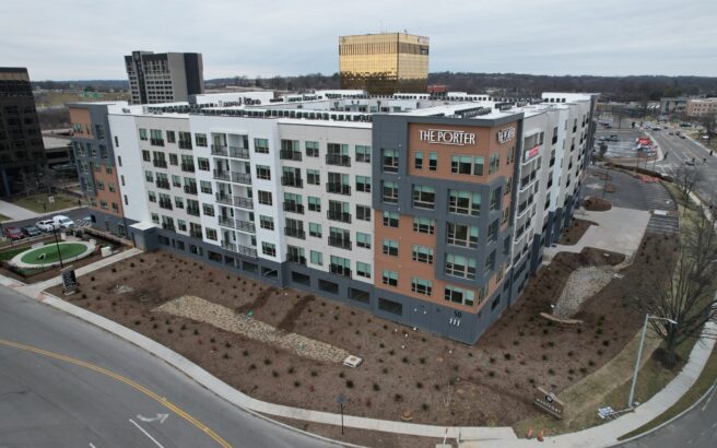 A modern, multi-story apartment building called The Porter stands on a street corner with landscaped surroundings and nearby office buildings under a cloudy sky.