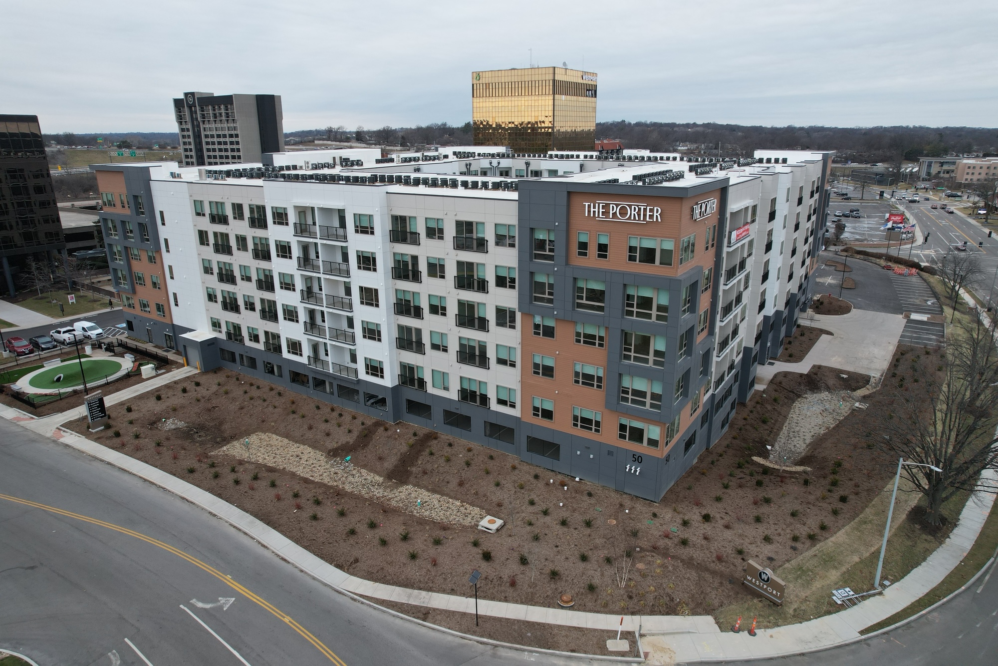 A modern, multi-story apartment building called The Porter stands on a street corner with landscaped surroundings and nearby office buildings under a cloudy sky.