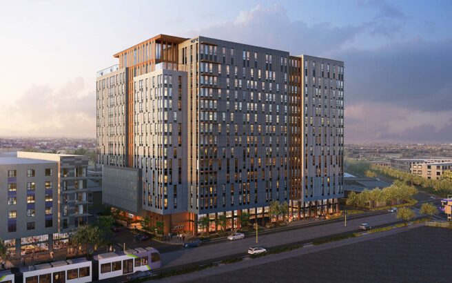 A modern high-rise apartment building with large windows and multiple floors stands by a busy street, surrounded by other buildings, trees, and parked cars under a partly cloudy sky.