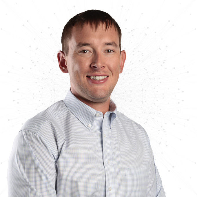 A man with short brown hair, wearing a light blue checkered button-up shirt, smiles at the camera against a white background with subtle dotted patterns.