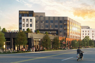 Modern multi-story apartment building labeled “RAMBLER” with large windows, greenery, and people on patios; a person on a scooter rides along the street in front under a partly cloudy sky at sunset.